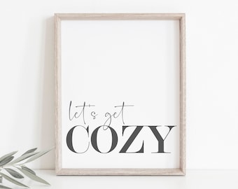 May include: A framed print with the text "Let's get cozy" in black lettering on a white background. The frame is a light wood color.