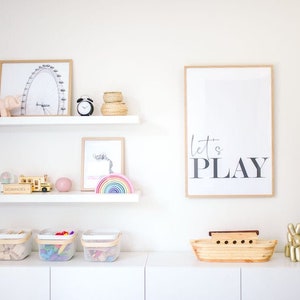 May include: White shelves with toys and decorations, including a wooden school bus, a rainbow stacking toy, a pink elephant figurine, a black alarm clock, and a framed print that says "Let's Play".