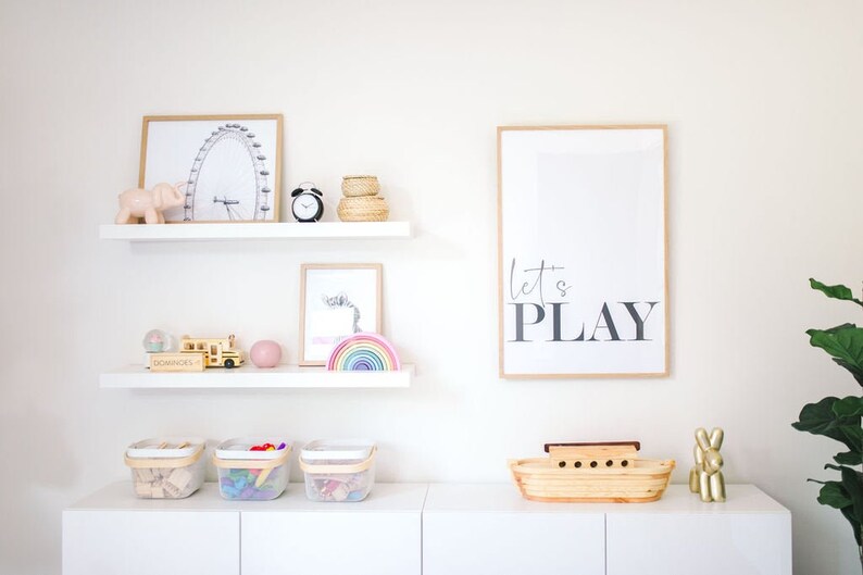 May include: White shelves with toys and decorations, including a wooden school bus, a rainbow stacking toy, a pink elephant figurine, a black alarm clock, and a framed print that says "Let's Play".