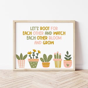 Puede incluir: Un estampado enmarcado con el texto "LET'S ROOT FOR EACH OTHER AND WATCH EACH OTHER BLOOM AND GROW". Debajo del texto hay ilustraciones de cinco plantas en macetas de varios estilos y colores. El marco es de color madera clara.