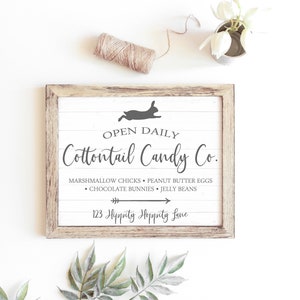 May include: A white wooden sign with a brown frame, featuring the text "OPEN DAILY Cottontail Candy Co." and a silhouette of a rabbit. The sign lists the candy shop's offerings: "Marshmallow Chicks, Peanut Butter Eggs, Chocolate Bunnies, Jelly Beans." The address is listed as "123 Hippity Hoppity Lane."