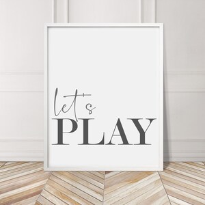 May include: A white framed print with the text "let's PLAY" in gray lettering on a white background.