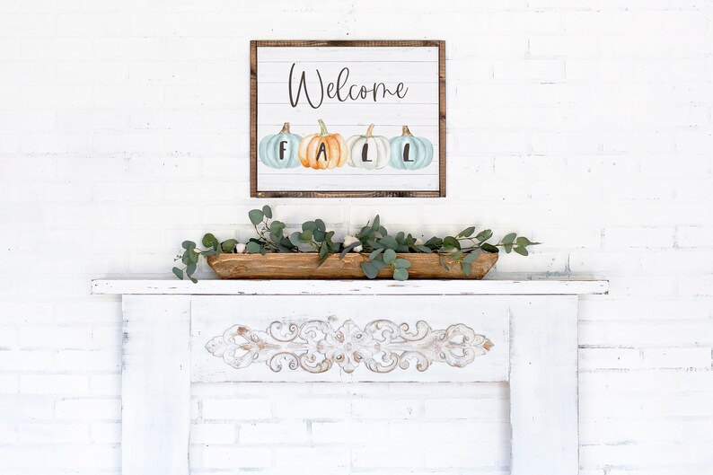 May include: A rectangular wall sign with a white shiplap background and a dark wood frame. The sign features the word Welcome in black script above four watercolour pumpkins in shades of blue and orange, each marked with the letters F, A, L, L.