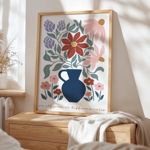 May include: A framed floral art print featuring a navy blue vase filled with stylized flowers in shades of red, pink, and purple. The print includes the text "we all grow at different rates" in a script font.