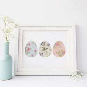 May include: A white frame with a white mat and a print of three pastel floral patterned Easter eggs. The print is on a white background.