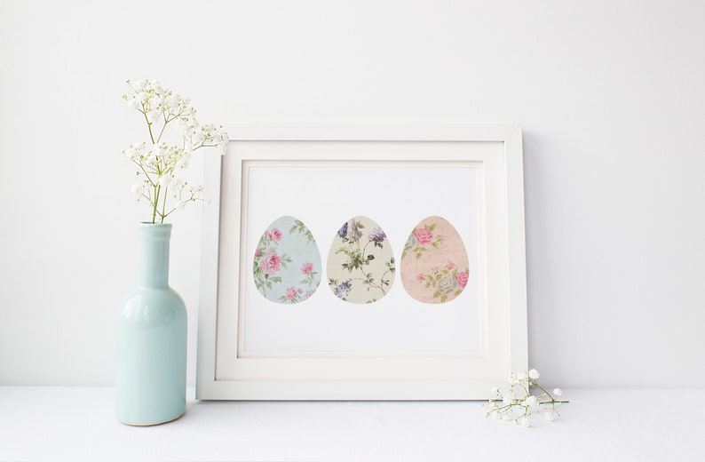 May include: A white frame with a white mat and a print of three pastel floral patterned Easter eggs. The print is on a white background.