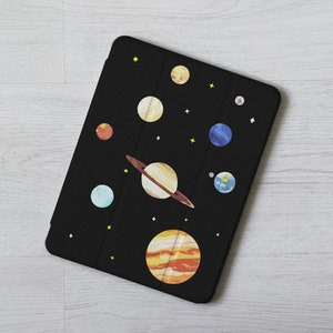 May include: A black tablet case featuring a design of planets and stars. The planets are in various colours, including yellow, orange, blue, and brown. The case has a textured surface.