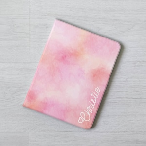 Puede incluir: Una funda para tablet con un diseño de acuarela rosa y naranja, con el nombre "Christie" escrito en cursiva blanca.