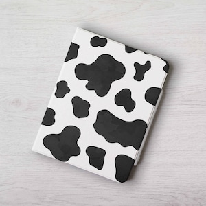 May include: A white tablet case featuring a black cow print pattern. The case is rectangular with rounded edges and a smooth finish. The black spots are of varying shapes and are spread across the white surface.