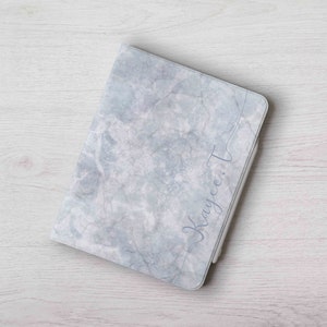 May include: A gray and white marble-patterned notebook cover with the name "Kaycee T" written in cursive on the front.