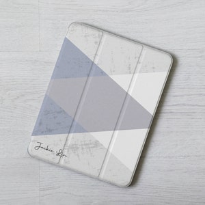 May include: A white tablet case with a geometric pattern in shades of grey and blue. The case has a signature that reads "Jackie Lin".