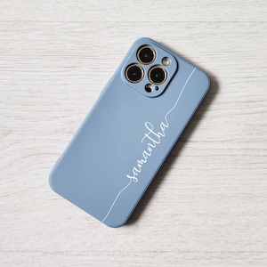 May include: A light blue phone case with a white inscription that says "Samantha". The case has a camera lens cutout with three black circles.