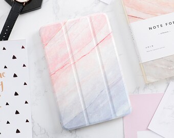 May include: A pink and white marble-patterned tablet case with a fold-over flap. The case has a subtle pink and white marble design.