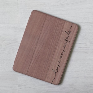 Peut inclure: Une coque de tablette en bois brun avec le texte "love never fails" écrit en cursive noire sur le côté.