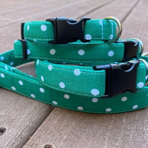 May include: Three green and white polka dot dog collars with black plastic buckles. The collars are stacked on top of each other.
