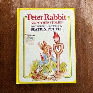 May include: A vintage copy of "Peter Rabbit and Other Stories" by Beatrix Potter. The cover features an illustration of Peter Rabbit eating carrots, a bird perched on a shovel, and the book's title in red. The book has a yellow border and a Target Books sticker.