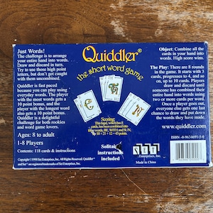 May include: The back of a Quiddler card game box, featuring the game's logo and instructions. The box is dark blue with white text and illustrations of cards. The game is for 1-8 players, ages 8 to adult.