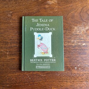 May include: A green hardcover book titled The Tale of Jemima Puddle-Duck by Beatrix Potter. The cover features a central illustration of a duck wearing a blue bonnet and a pink shawl, with the text The Original and Authorized Edition F. Warne & Co.