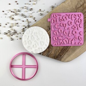 Pode incluir: Um conjunto de ferramentas de fondant rosa para decorar bolos e biscoitos. O conjunto inclui um cortador redondo, uma ferramenta de embossing de estampa de leopardo e um tapete de impressão de estampa de leopardo.