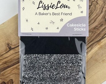 以下が含まれることがあります： 銀色のグリッターケーキシクルスティックのパッケージ。パッケージは黒の背景で、前面に「Lissie Lou」と「A Baker's Best Friend」の文字が書かれています。「Cakesicle Sticks」の文字もパッケージの前面にあります。