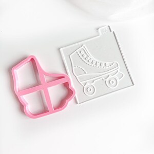 Puede incluir: Un cortador de galletas de plástico rosa en forma de patines y una plantilla de plástico transparente en forma de patines.