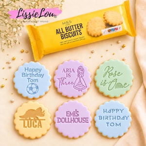 May include: A yellow packet of M&S All Butter Biscuits and six round scalloped biscuits with embossed designs. The biscuits feature text including Happy Birthday Tom, Aria Is Three, Rose Is One, Luca, Emi's Dollhouse, and a second Happy Birthday Tom.