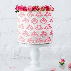 May include: A white cake decorated with a pink and white shell pattern. The cake is on a white cake stand and is surrounded by pink rose petals.