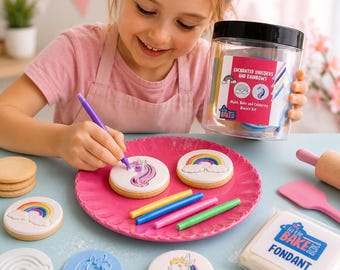 Puede incluir: Un kit de decoración de galletas con un tarro de plástico transparente etiquetado como Enchanted Unicorns and Rainbows, un plato rosa festoneado, galletas redondas con diseños de unicornios y arcoíris, rotuladores comestibles y fondant blanco.