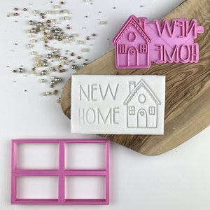 Op de afbeelding: Een set roze plastic koekjesvormen om te bakken. De vormen zijn in de vorm van een huis met de woorden "NEW HOME" en een vensterframe.