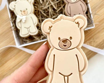 Può includere: Tre biscotti a forma di orsacchiotto marrone e beige in una scatola regalo. I biscotti sono decorati con semplici tratti del viso.