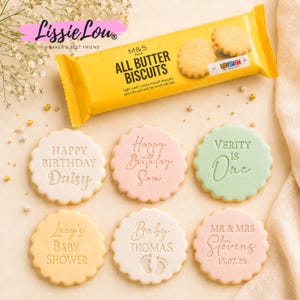 Könnte beinhalten: Eine gelbe Packung M&S Food All Butter Biscuits über sechs runden Keksen mit gewelltem Rand und geprägtem Text. Die Kekse zeigen Botschaften wie Happy Birthday Daisy, Happy Birthday Sam, Verity is One, Lucy's Baby Shower, Baby Thomas mit Fußabdrücken und Mr & Mrs Stevens 15.07.26.