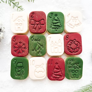 Könnte beinhalten: Ein Dutzend quadratischer Weihnachtsplätzchen mit geprägten Designs und Zahlen von 1 bis 12. Die Motive umfassen ein Haus, eine Schleife, einen Weihnachtsbaum, Glocken, einen Schneeflocke, Mistelzweige, Kerzen, einen Kranz, einen Schneemann, eine Geschenktüte und ein Haus.