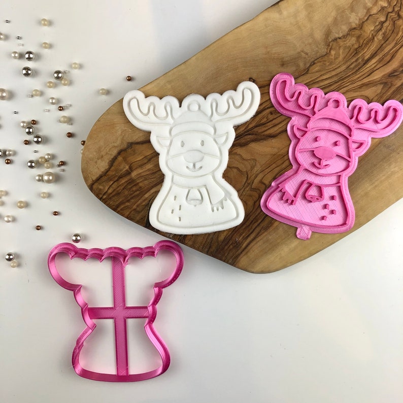 May include: Two white and pink plastic reindeer cookie cutters. The reindeer have a bell on their scarf and a Santa hat. There is also a pink plastic cookie cutter shaped like a bell.