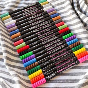 Puede incluir: Una colecci&oacute;n de rotuladores comestibles de doble punta LissieLou en varios colores, incluyendo turquesa met&aacute;lico, oro, plata, blanco, morado, bronce, azul, oro rosa, gris, negro, rosa, verde, rojo, naranja y marr&oacute;n, cada uno con su nombre de color.