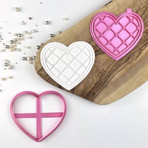 May include: Three pink heart-shaped cookie cutters. One cutter has a diamond pattern, one has a simple cross design, and the other is plain.