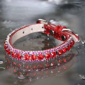 Puede incluir: Un collar de perro de cuero rojo con una doble fila de piedras de imitación rojas y rosas.