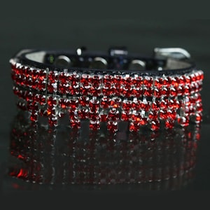 Puede incluir: Un collar de perro de cuero negro con tres filas de adornos de diamantes de imitación rojos.