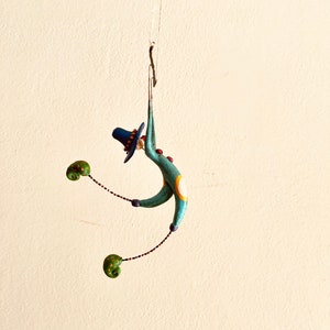Può includere: Una figurina stravagante di un clown blu e verde appeso al soffitto. Il clown indossa un cappello blu e ha un cerchio giallo sul corpo. Il clown tiene due guantoni da boxe verdi.