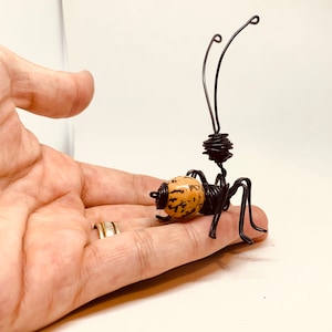 Puede incluir: Una escultura de alambre hecha a mano de una hormiga. La hormiga tiene un cuerpo marr&oacute;n y beige, patas de alambre negro y antenas. La escultura es una obra de arte &uacute;nica.