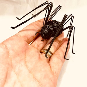 Puede incluir: Una escultura de ara&ntilde;a de alambre negro con patas largas. La ara&ntilde;a est&aacute; sentada en la mano de una persona.