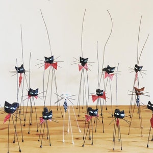 Puede incluir: Una colecci&oacute;n de figuritas de gatos negros con pajaritas rojas y patas largas y delgadas de alambre. Los gatos est&aacute;n dispuestos sobre una superficie de madera.
