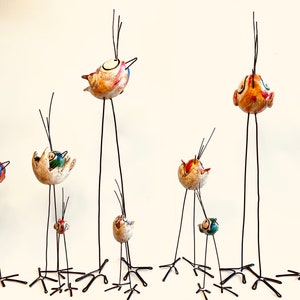 Puede incluir: Una colecci&oacute;n de nueve p&aacute;jaros de cer&aacute;mica caprichosos con detalles coloridos, posados ​​en patas de alambre delgadas y altas. Cada p&aacute;jaro tiene un dise&ntilde;o y una expresi&oacute;n &uacute;nicos, lo que agrega un toque l&uacute;dico a cualquier decoraci&oacute;n.