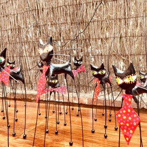 Puede incluir: Un grupo de figuritas de gatos negros con patas largas y delgadas y pajaritas de lunares rojos y blancos. Los gatos est&aacute;n dispuestos en fila sobre una superficie de madera.