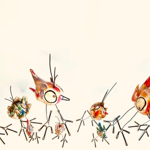 Puede incluir: Un grupo de p&aacute;jaros de cer&aacute;mica pintados a mano con patas de alambre. Los p&aacute;jaros est&aacute;n en varias poses, algunos con las alas extendidas y otros con la cabeza inclinada. Los p&aacute;jaros est&aacute;n pintados en colores brillantes, incluyendo rojo, amarillo, azul y verde.
