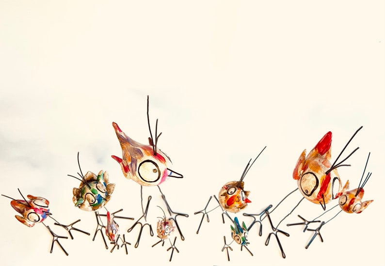 Puede incluir: Un grupo de p&aacute;jaros de cer&aacute;mica pintados a mano con patas de alambre. Los p&aacute;jaros est&aacute;n en varias poses, algunos con las alas extendidas y otros con la cabeza inclinada. Los p&aacute;jaros est&aacute;n pintados en colores brillantes, incluyendo rojo, amarillo, azul y verde.