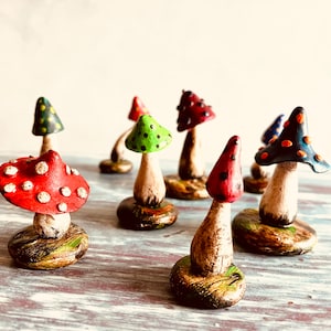 Puede incluir: Una colecci&oacute;n de setas en miniatura hechas a mano con dise&ntilde;os de lunares coloridos. Las setas est&aacute;n hechas de arcilla y pintadas en varios colores, incluyendo rojo, verde, azul y negro. Cada seta tiene un dise&ntilde;o &uacute;nico y se muestra en una peque&ntilde;a base.