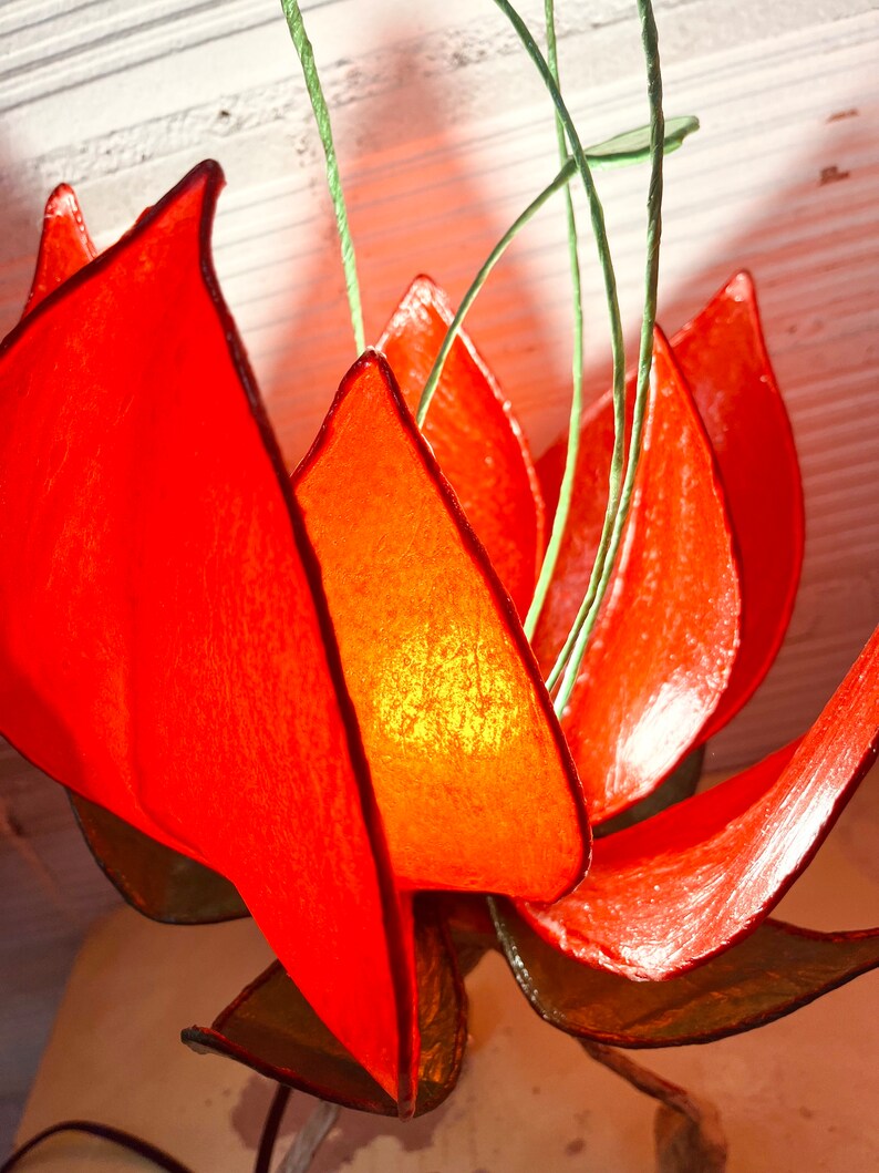 Puede incluir: Una l&aacute;mpara de papel con forma de flor roja con tallos verdes. La l&aacute;mpara est&aacute; encendida y la luz brilla a trav&eacute;s del papel.