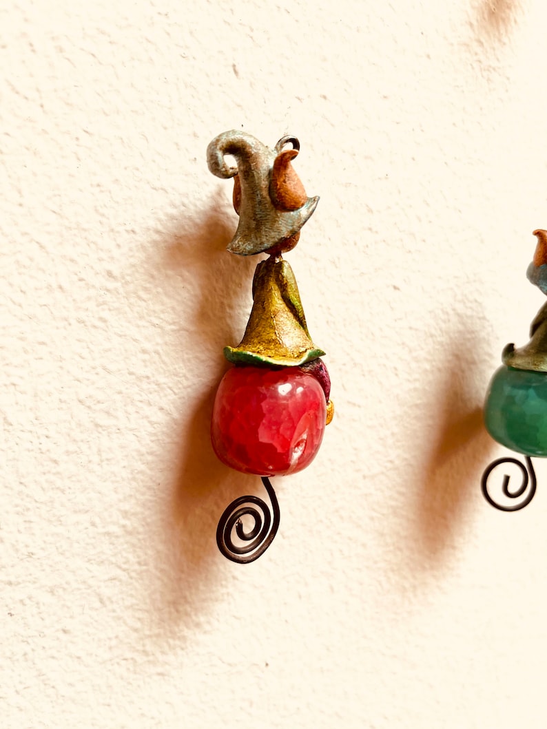 May include: A whimsical gnome figurine with a red and green hat, a pink and green body, and a curled wire tail.