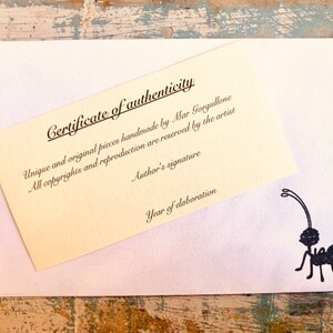 May include: A certificate of authenticity for a handmade piece. The certificate is printed on a cream-colored paper with black text. The text reads "Certificate of authenticity", "Unique and original pieces handmade by Mar Gorgullone", "All copyrights and reproduction are reserved by the artist", "Author's signature", and "Year of elaboration".