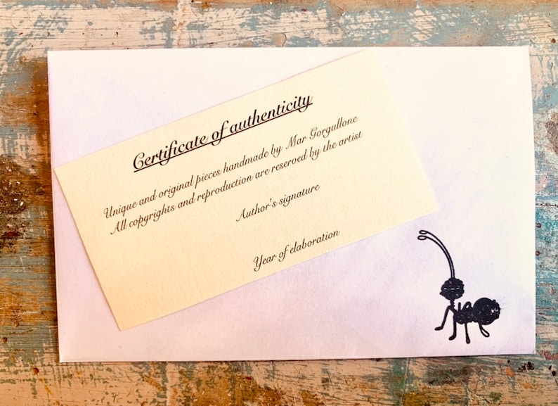 May include: A certificate of authenticity for a handmade piece. The certificate is printed on a cream-colored paper with black text. The text reads "Certificate of authenticity", "Unique and original pieces handmade by Mar Gorgullone", "All copyrights and reproduction are reserved by the artist", "Author's signature", and "Year of elaboration".